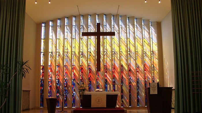 Die Kirche mit einem großen Kreuz vor buntem Glasfenster