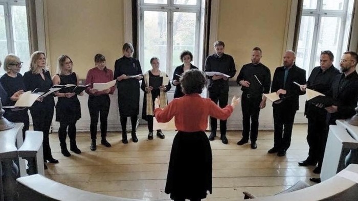 En gruppe af mænd og kvinder synger i en sal med en dirigent i forgrunden