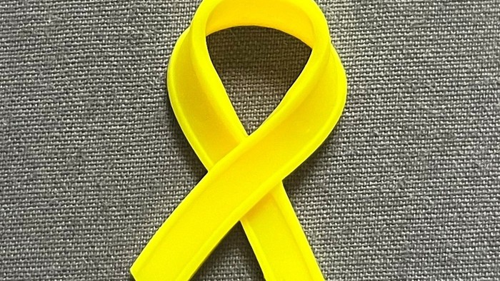 Eine gelbe Schleife auf einem grauen Stoff.