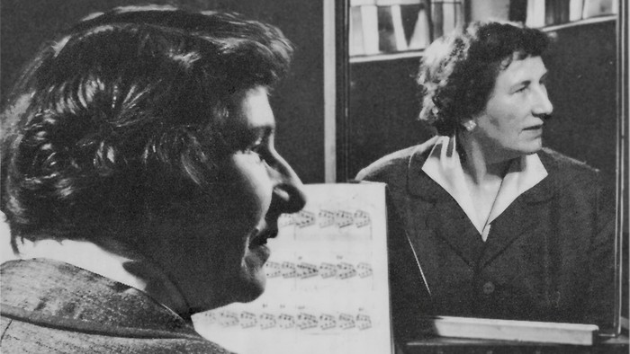 Zwei Personen führen gemeinsam ein Musikstück auf, wobei eine Person Notenblätter liest und Klavier spielt.