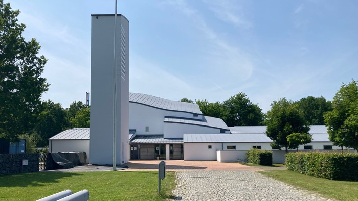 Moderne kirke med høj tårn og fladt tag i grøn omgivelse