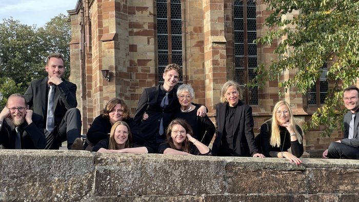 Ein Gruppe von Menschen sitzt vor einem alten Gebäude und posiert für ein Foto.