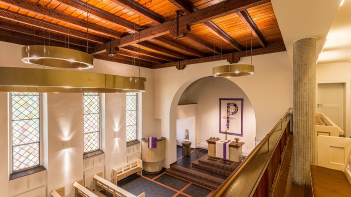 Das Bild zeigt einen großen Raum mit Holzbalkendecke, einem Treppenhaus und einem großen "P"-Wanddekoration.