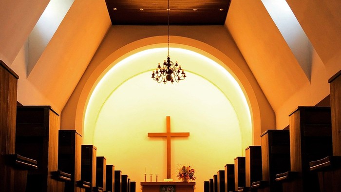 Die Kirche mit Holzpulten und einem großen Kreuz im Altarraum.