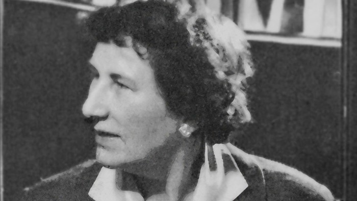 Ein Porträt einer Frau aus der Mitte des 20. Jahrhunderts in einer Bluse mit Kragen und Strickjacke, nachdenklich blickend.