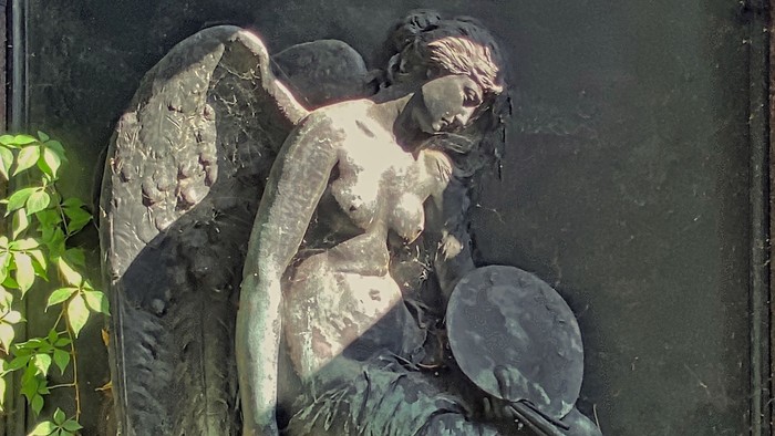 Eine bronzene Statue einer engelhaften Figur, die einen Spiegel hält, verziert mit einem Lorbeerkranz-Porträt darüber.