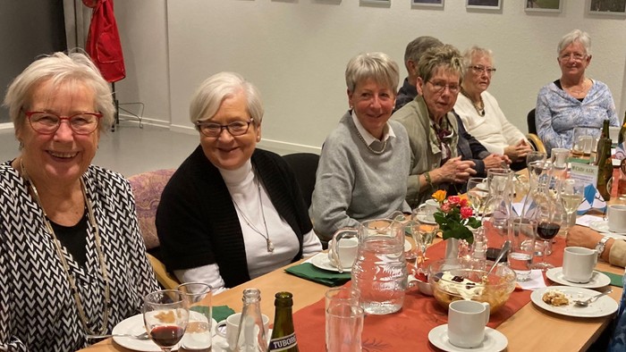 En gruppe pensionister sidder sammen ved et bord med mad og drikkevarer.