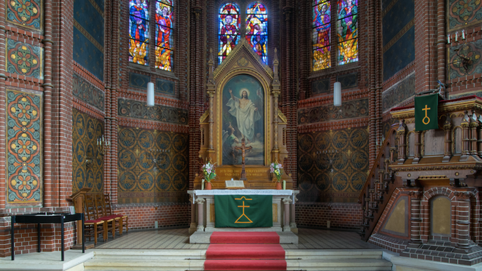 Innenraum einer Kirche mit Altar, farbenfrohen Fenstern und Teppichen