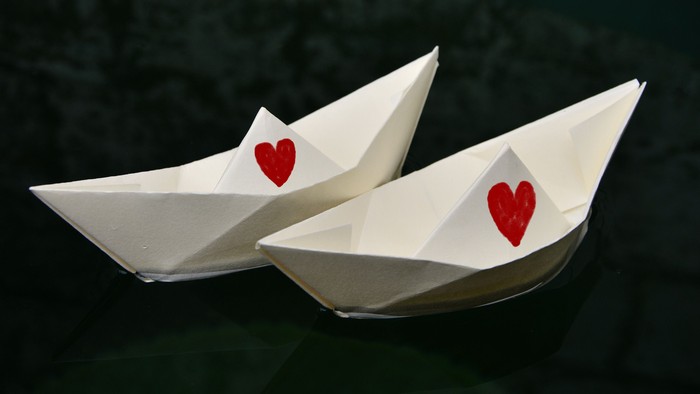 Zwei Origami-Boote mit Herzchen auf grünem Hintergrund