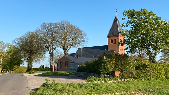 En lille kirke med tårn og et hvidt sidebygning i landlig omgivelse