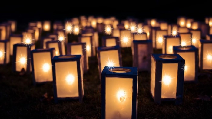 Viele beleuchtete Laternen stehen im Dunkeln auf einem Feld.