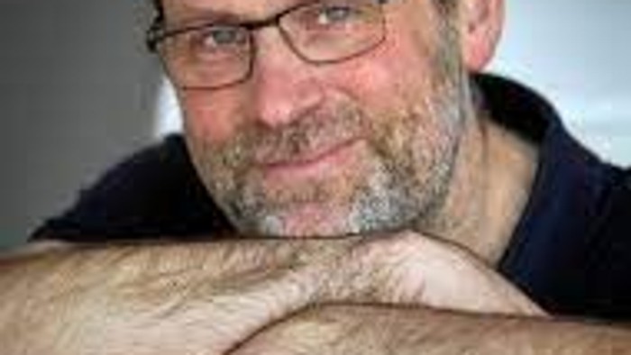 En bart og brillet mand med briller sidder og har armene krydset.