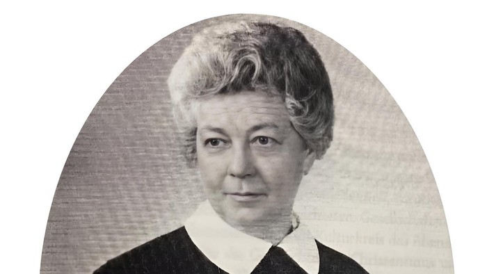 Eine ältere Frau hält ein Buch und trägt eine Bluse mit Kragen.