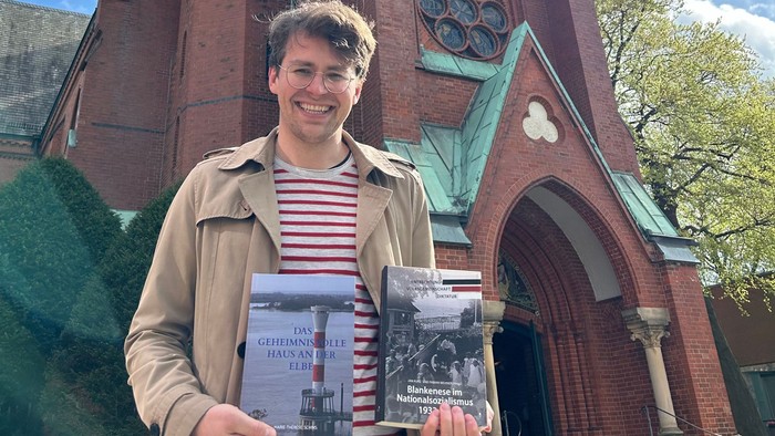 Junger Mann hält zwei Bücher vor Kirche