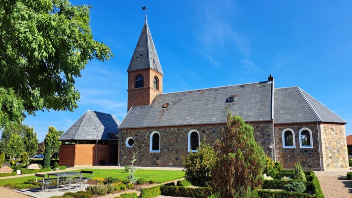 En lille kirke med tårn og omgivelser med græsplæne og træer