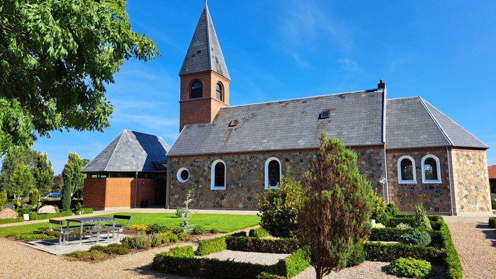 En lille kirke med tårn og omgivelser med græsplæne og træer