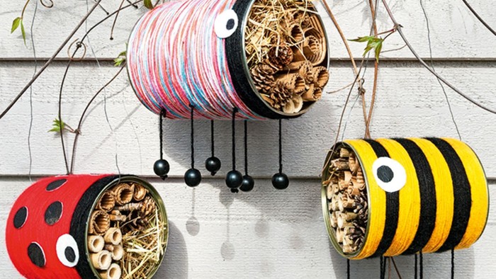 Drei bunte Vogelhäuschen in Form von Marienkäfern und einer Biene hängen an einer Wand.