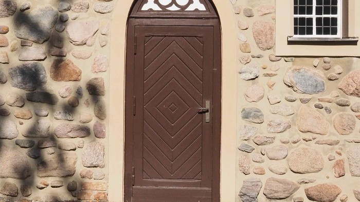 Das Bild zeigt eine hölzerne Tür in einem steinernen Gebäude.