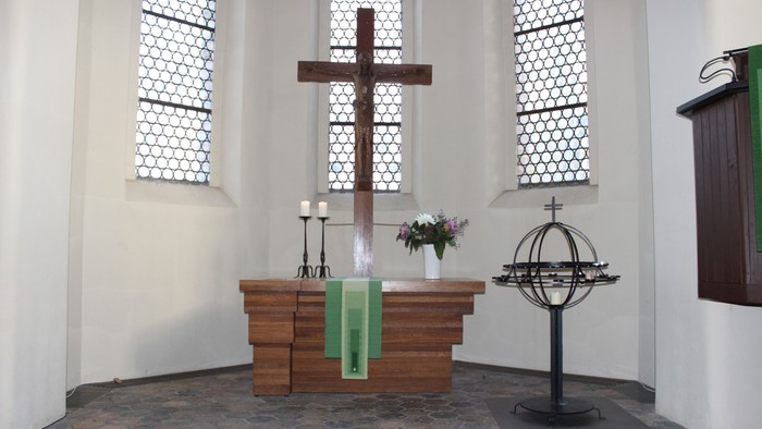 In der Kirche: Altar mit Kreuz, Kerzen und Blumen, daneben ein Globus.