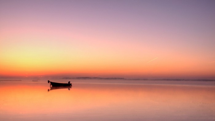 En lille båd på vand ved solopgang