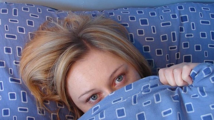 En kvinde med rødt hår ligger i sengen og kigger op.