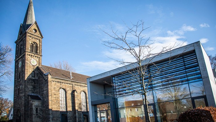 Altes Kirchengebäude neben moderner Glasfassade unter blauem Himmel
