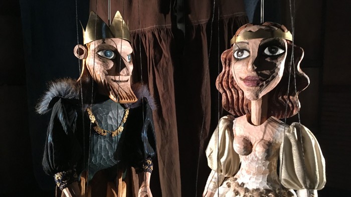 To marionetter, en konge og en dronning, hænger i mørkt teater.