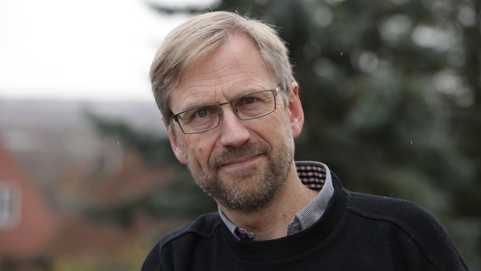 En mand med blond hår og briller står ude ved et træ.