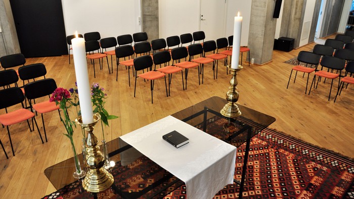 En lille kapel med sorte stoler og to lysestage på alteret.