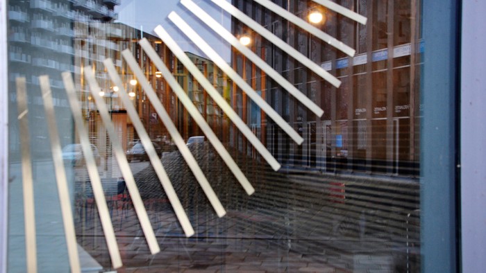 Glasfasade med reflekser af lys og bygning.