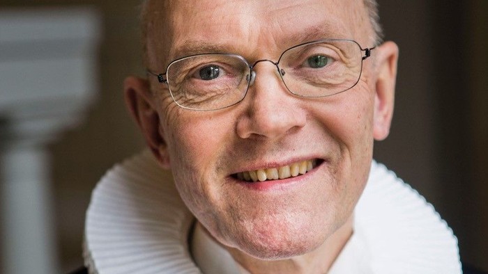 En smilende, eldre mand med glas og en hvid krage.