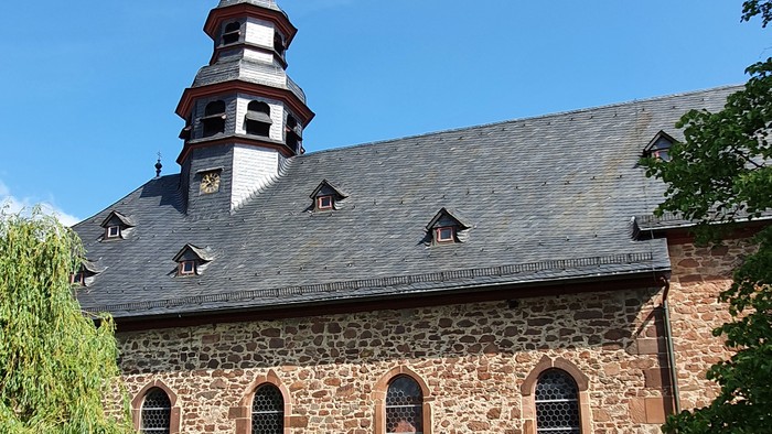 Alte Kirche mit hohem Turm und spitzem Dach, umgeben von Bäumen und grünem Gras