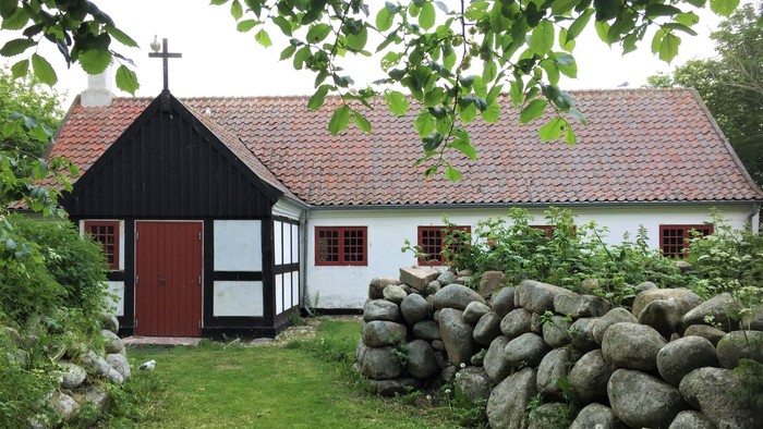 En lille sort og hvid hus med røde tag og dør, omgivet af græs og stenmure