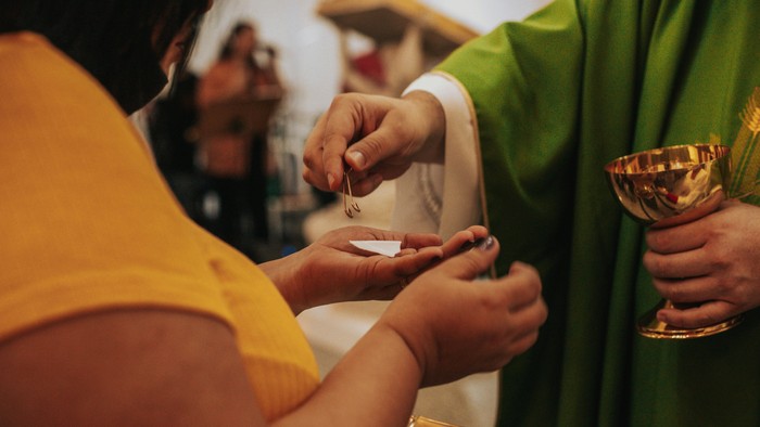 Ein Priester segnet ein Kind mit einem Kreuz und einer Schale.