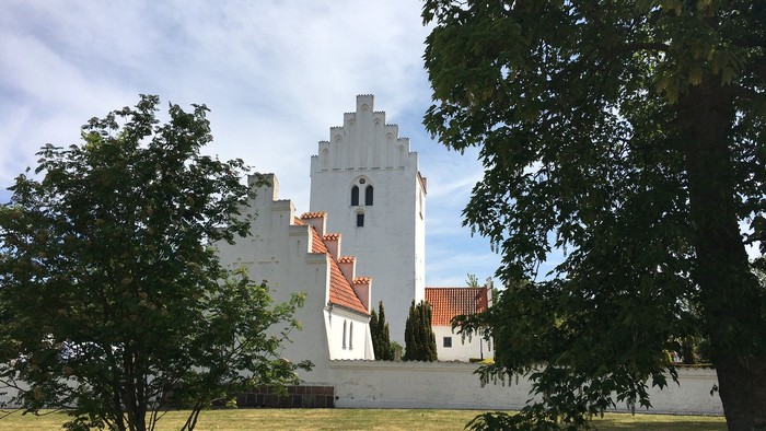 Et hvidt tårn med røde tag i træernes skygge