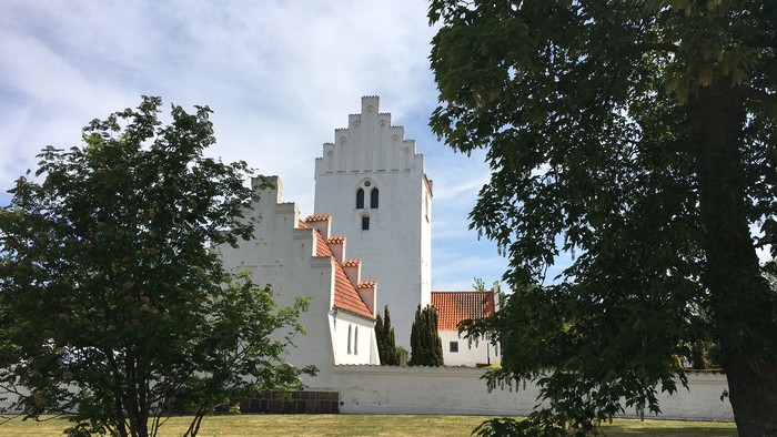 Et hvidt tårn med røde tag i træernes skygge