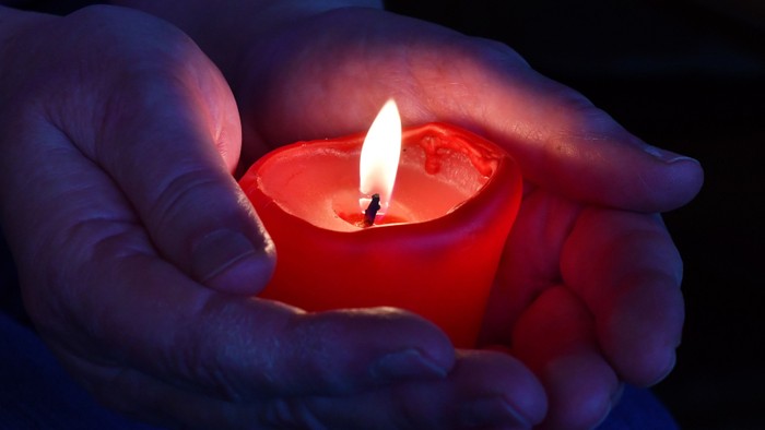 Eine Hand hält eine brennende rote Kerze im Dunkeln.
