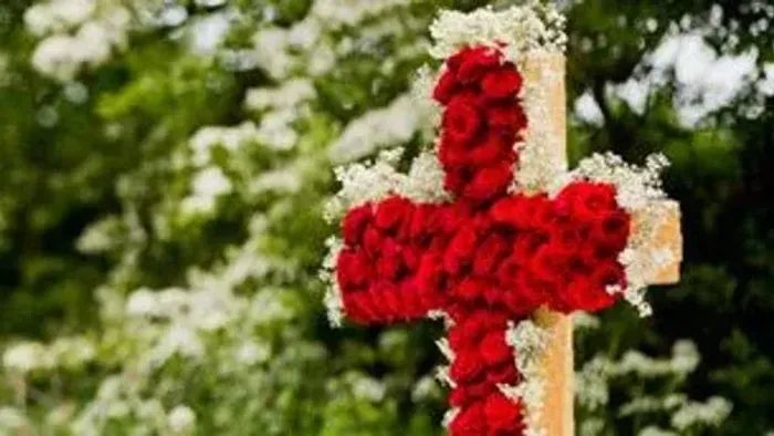 En rød krans i form af et kors på en stok med grønne træer i baggrunden