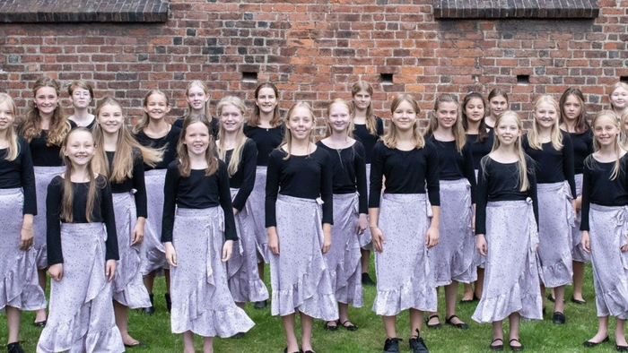 En gruppe kvinder i svart og hvidt tøj står sammen foran murstenge væg