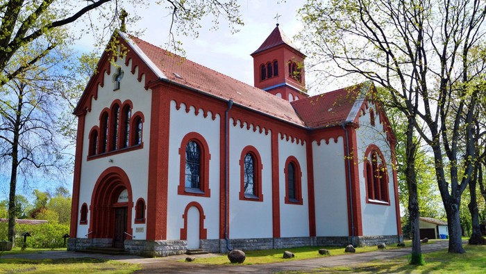 Das Bild zeigt eine rote und weiße Kirche mit einem Glockenturm, umgeben von Bäumen.