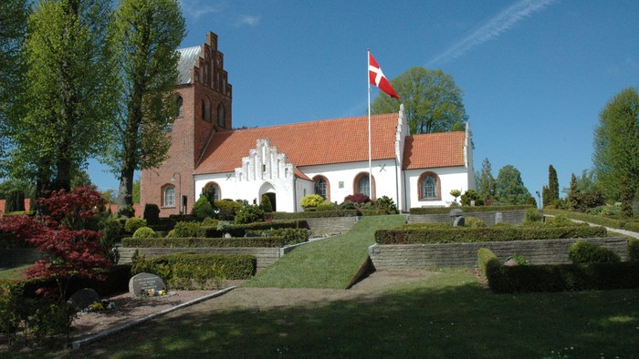 En hvid kirke med røde tag og en flagstang med et rødt flag foran