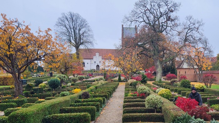 En park med formede buske og farverige blomsterbænker foran et historisk slot