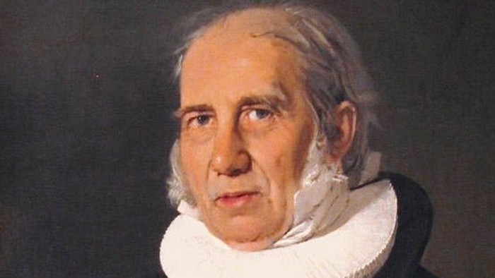 Portrait of an elderly man in black attire with white collar and medal.