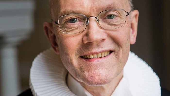 En smilende, eldre mand med glas og en hvid krage.