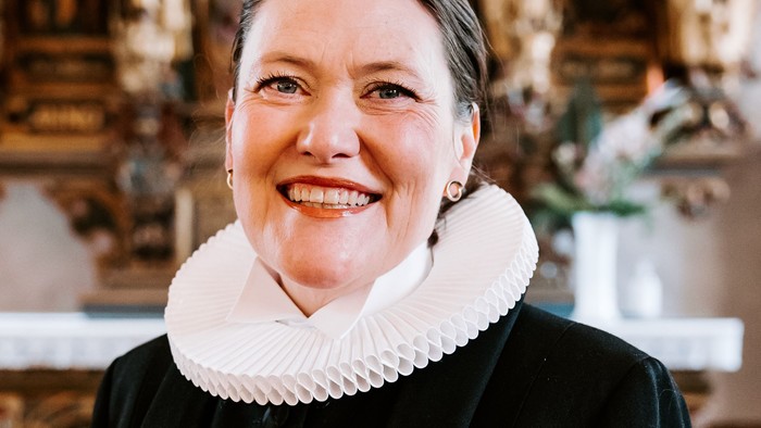 En kvinde i sort jakke med hvid krage står foran en prægtig altertavle.