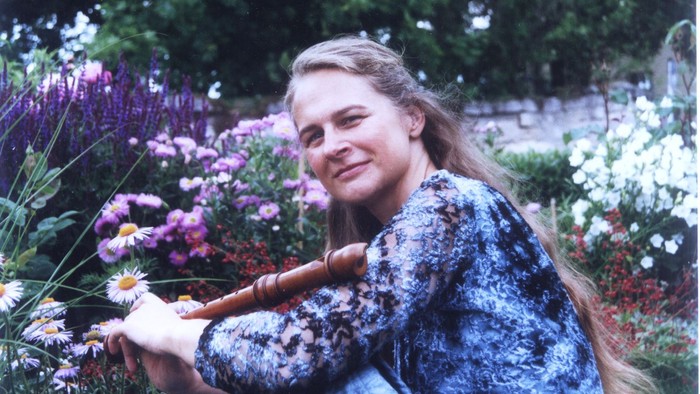 Eine Frau sitzt in einem Garten voller bunter Blumen und lächelt.