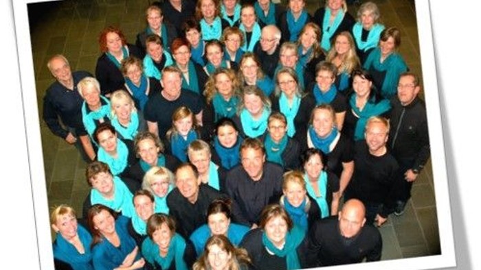 En stor gruppe af korister i blå og sorte uniformer samlet til et foto