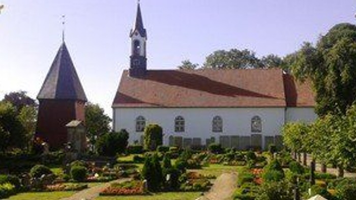 Weiße Kirche mit hohem Turm und rotem Dach in gepflegtem Garten.
