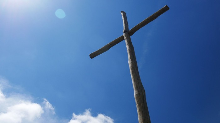 Ein hölzernes Kreuz vor blauem Himmel und Sonne.