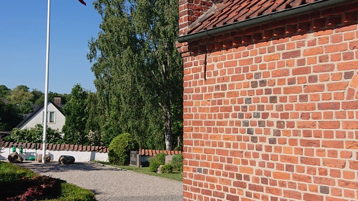 Røde mursten og flagstang med dansk flag ved rød tagget murstenhus